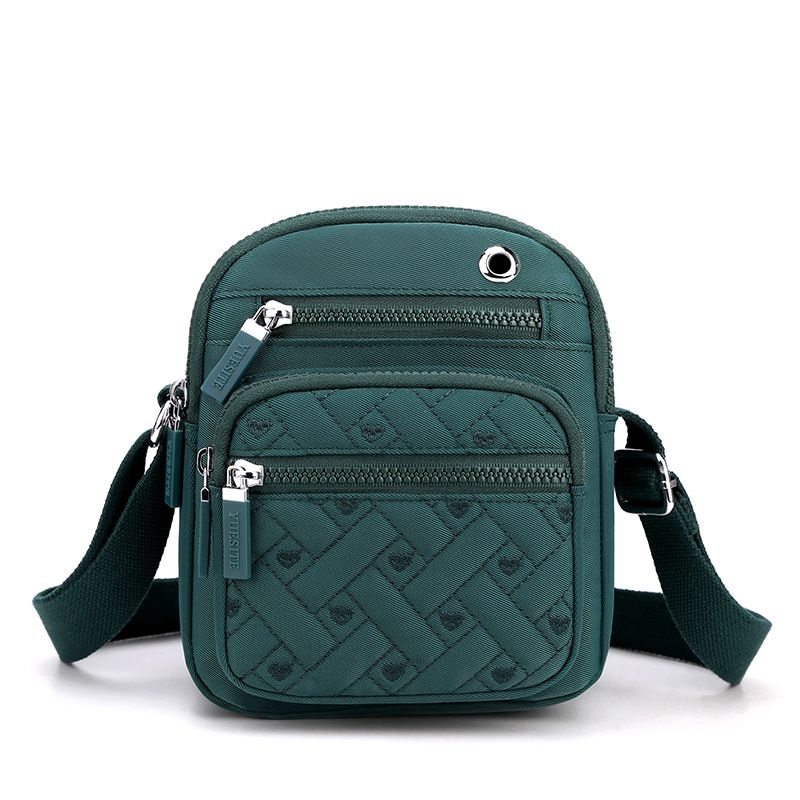 Crossbody nylon canvas bag in solid color teal with quilted geometric pattern, multiple zip pockets and strap.